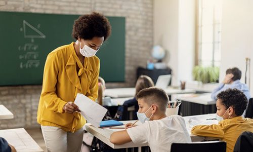 African American explaining test results to a schoolboy during a class. They are wearing protective face masks due to COVID-19 pandemic.